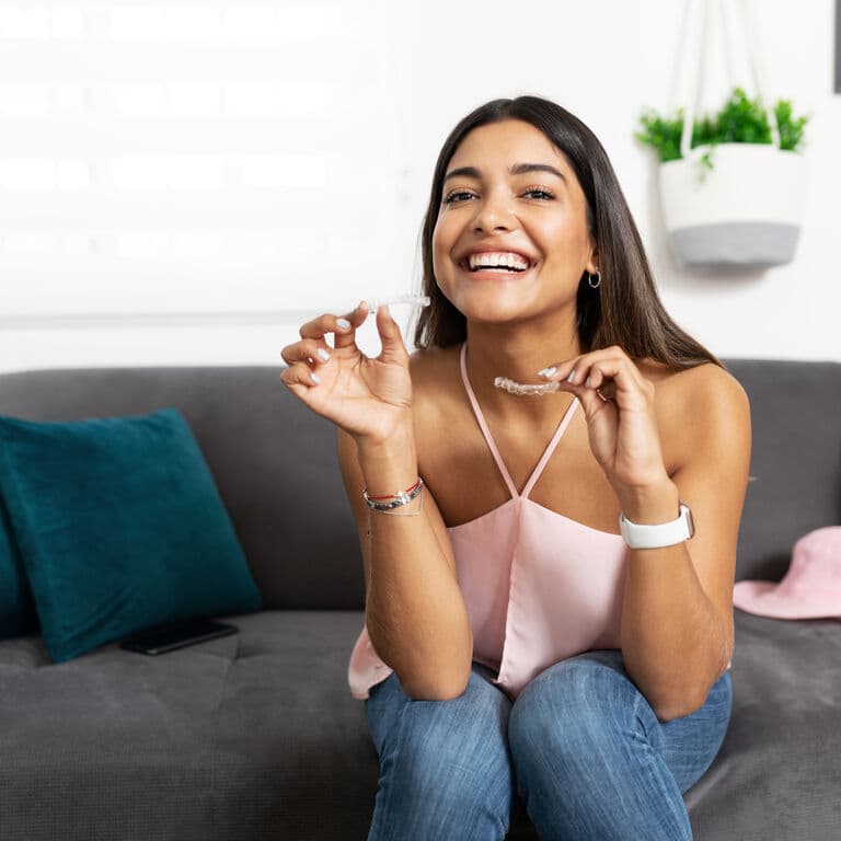 Patient smiling at home, holding her Invisalign aligners