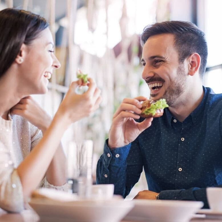 Couple laughing together over lunch, both with confident smiles