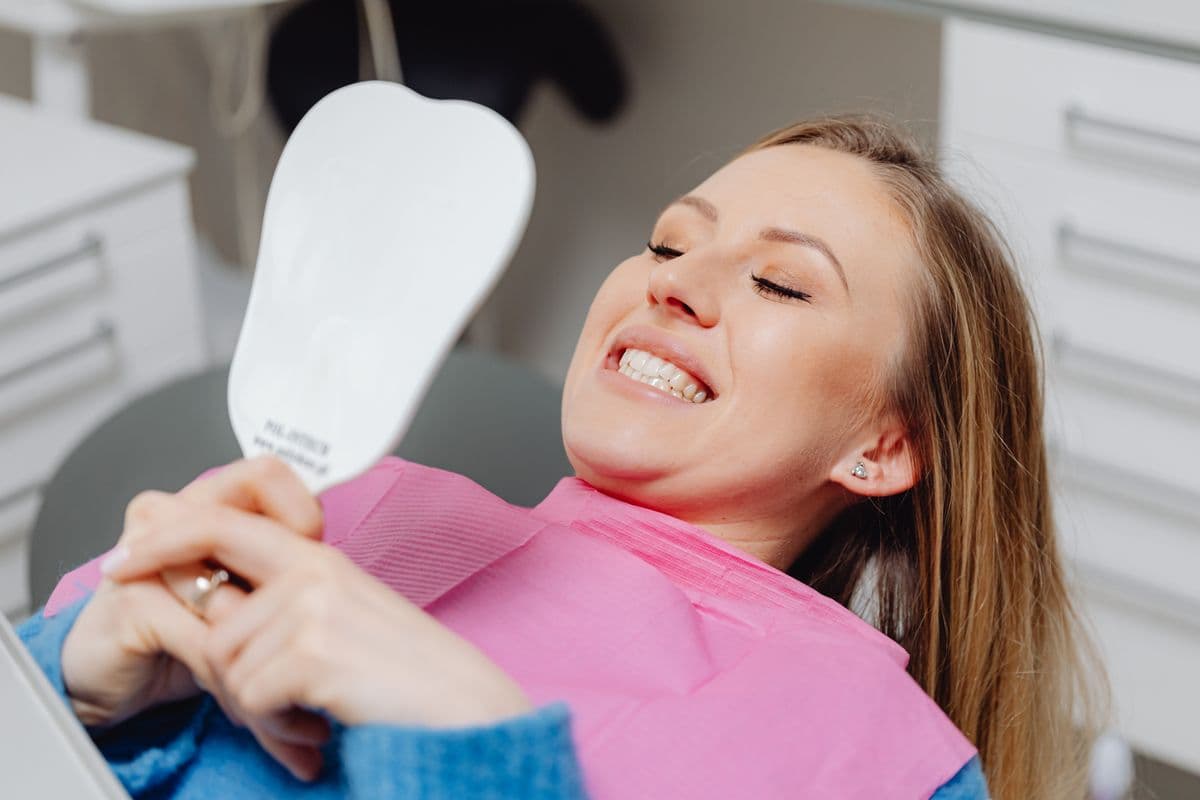 Woman checking her bright, white smile in a mirror after whitening treatment